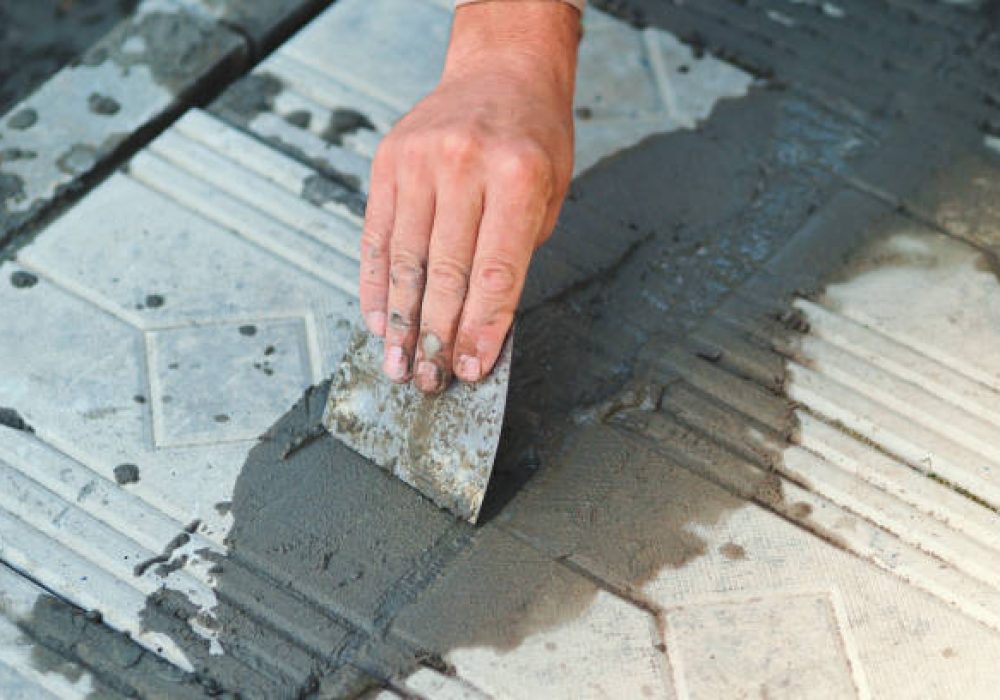 A carpenter repairs a building with tools at a construction site. The tiler lays out the tiles. Hand with a trowel close-up. Rubs cement paving slabs.
