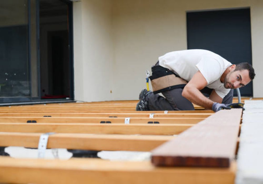 handsome young man carpenter installing a wood floor outdoor terrace in new house construction site